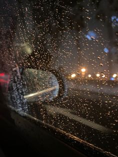 rain drops on the windshield of a car as it drives down a street at night