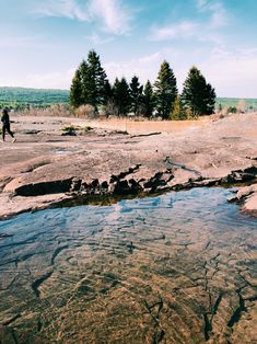 a man standing on top of a rock covered hillside next to a small creek filled with water