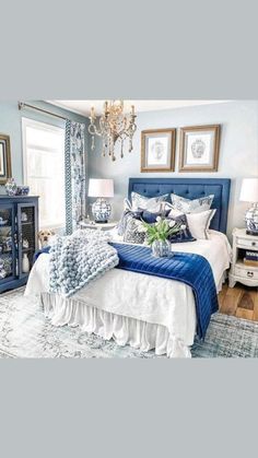 a blue and white bedroom with chandelier, bed, pillows, rugs and pictures on the wall