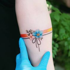 a person in blue gloves holding up a flower tattoo on their left arm and wrist