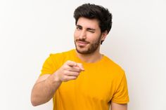 a man in a yellow shirt pointing to his left with one hand and looking at the camera