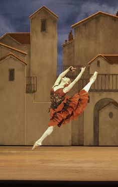 a ballerina in an orange dress is doing a trick on the stage with her arms stretched out