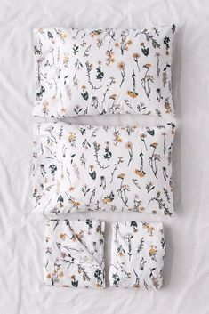 three pillows and two pillow cases on top of a white bed sheet with yellow flowers