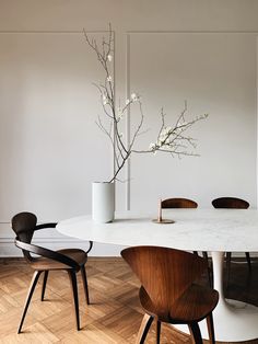 a dining room table with chairs and a vase on top of it in front of a white wall