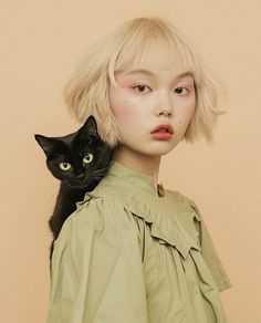 a woman with blonde hair and green eyes holding a black cat in her arms, looking at the camera