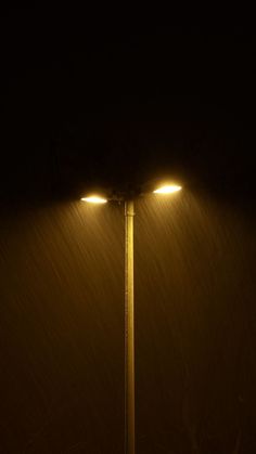 two street lights in the dark with snow falling on them and one light shining brightly