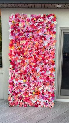 a large piece of art made out of flowers on the side of a building with a door