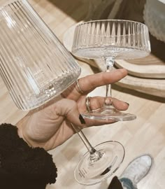 a person holding a wine glass in their hand with a lamp on the table behind them