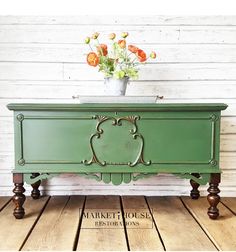 a green dresser sitting on top of a wooden floor next to a vase with flowers