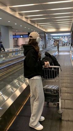 a woman with headphones standing in front of an empty shopping cart at the airport