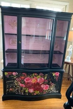 a black china cabinet with pink flowers painted on the front and side panels, sitting in a living room