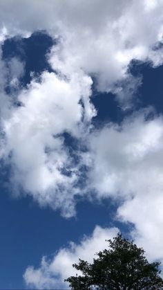 an airplane is flying in the blue sky with clouds and trees around it, as well as a tree