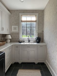 a kitchen with white cabinets and gray tile flooring next to a window that has a black vase on it