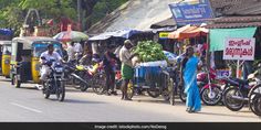 many people are riding motorcycles down the street in front of some shops and vendors with umbrellas over their heads