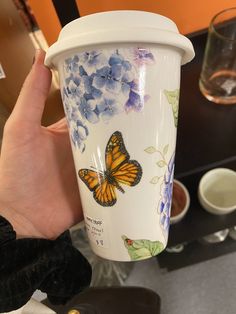 a hand holding a coffee cup with a butterfly painted on the side and blue flowers