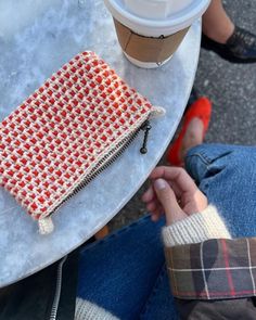 a person is sitting at a table with a cup of coffee and a purse on it