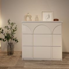 a white cabinet sitting next to a potted plant on top of a wooden floor