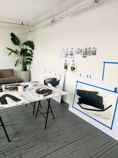 two tables with paintings on them in front of a white brick wall and wooden floor