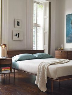 a bed sitting in a bedroom next to a wooden table with a lamp on top of it