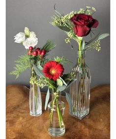 three vases with flowers in them sitting on a wooden table next to each other