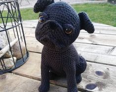 a crocheted black dog sitting on top of a wooden table next to a birdcage