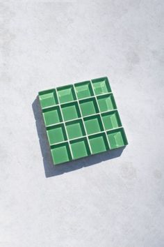 a green square shaped object sitting on top of a cement floor next to a white wall