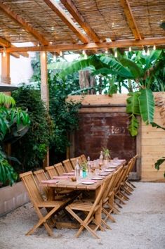 an outdoor dining area with wooden tables and chairs, surrounded by greenery in the background