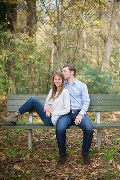 a man and woman are sitting on a bench in the fall leaves, smiling at each other