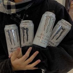 a person holding four cans of monster energy drink in their hands, with one hand on the other