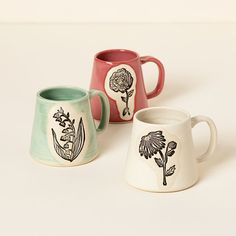 three mugs with designs on them sitting next to each other, one has a flower in the middle