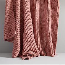 a pink knitted blanket hanging on a wall