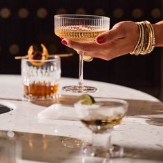 a person holding a wine glass over a table with two glasses on top of it