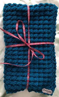 a blue crocheted blanket with a red ribbon tied around the edge and on top of it