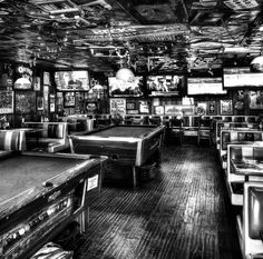 a black and white photo of a pool table in a room with many tvs