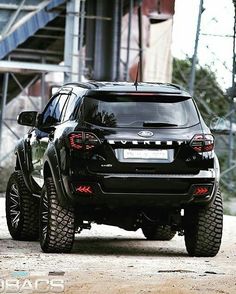 the rear end of a black suv parked in front of a large metal structure with stairs leading up to it