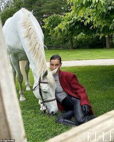 a woman kneeling down next to a white horse on top of a lush green field