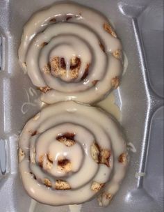 two glazed donuts with icing in a plastic container