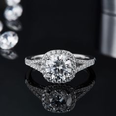 an engagement ring with diamonds around it on a black surface next to other jewelry items