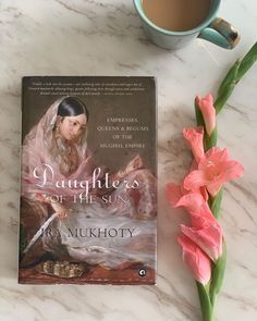 a book sitting on top of a table next to a cup of coffee and pink flowers