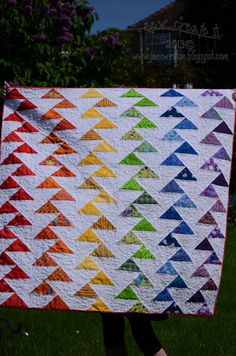 a person holding up a colorful quilt in the grass