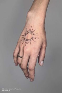 a person's hand with a small sun tattoo on it