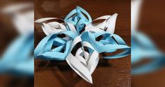 an origami snowflake made out of blue and white paper on a wooden table