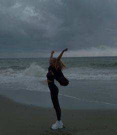 a woman standing on one leg in front of the ocean