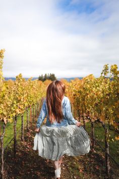 a woman in a dress walking through a vineyard