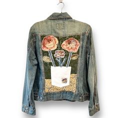 a jean jacket with flowers on it hanging from a hook and some clothes pins in the pocket