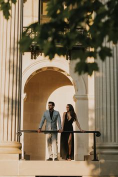 a man and woman are walking down the stairs in front of a building with columns