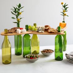 several green bottles with food and flowers in them on a white countertop next to plates