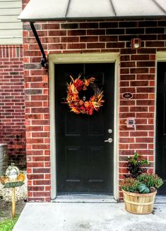 a black door with a wreath on it and two plants in front of the door