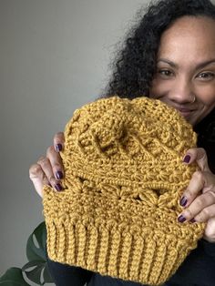 a woman holding up a yellow knitted object