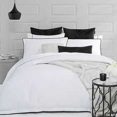 a bed with white sheets and black pillows in a room next to a lamp on a table